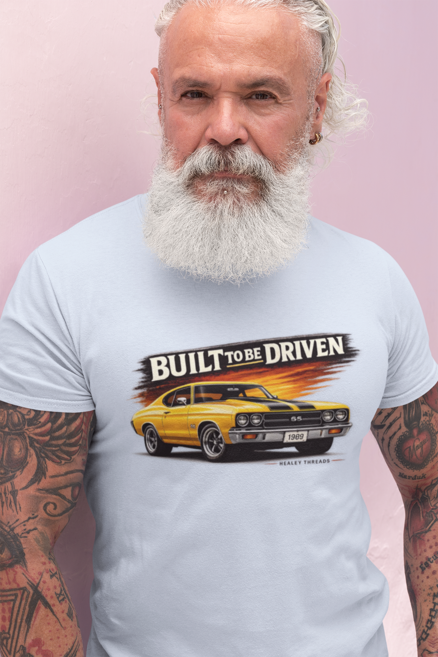 Man wearing a white t-shirt with a graphic of a yellow car and text 'Built to be Driven' on a pink background