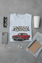 Light blue t-shirt with red car graphic and 'No Garage Queens' text on a gray surface with phone, glasses, and newspaper.