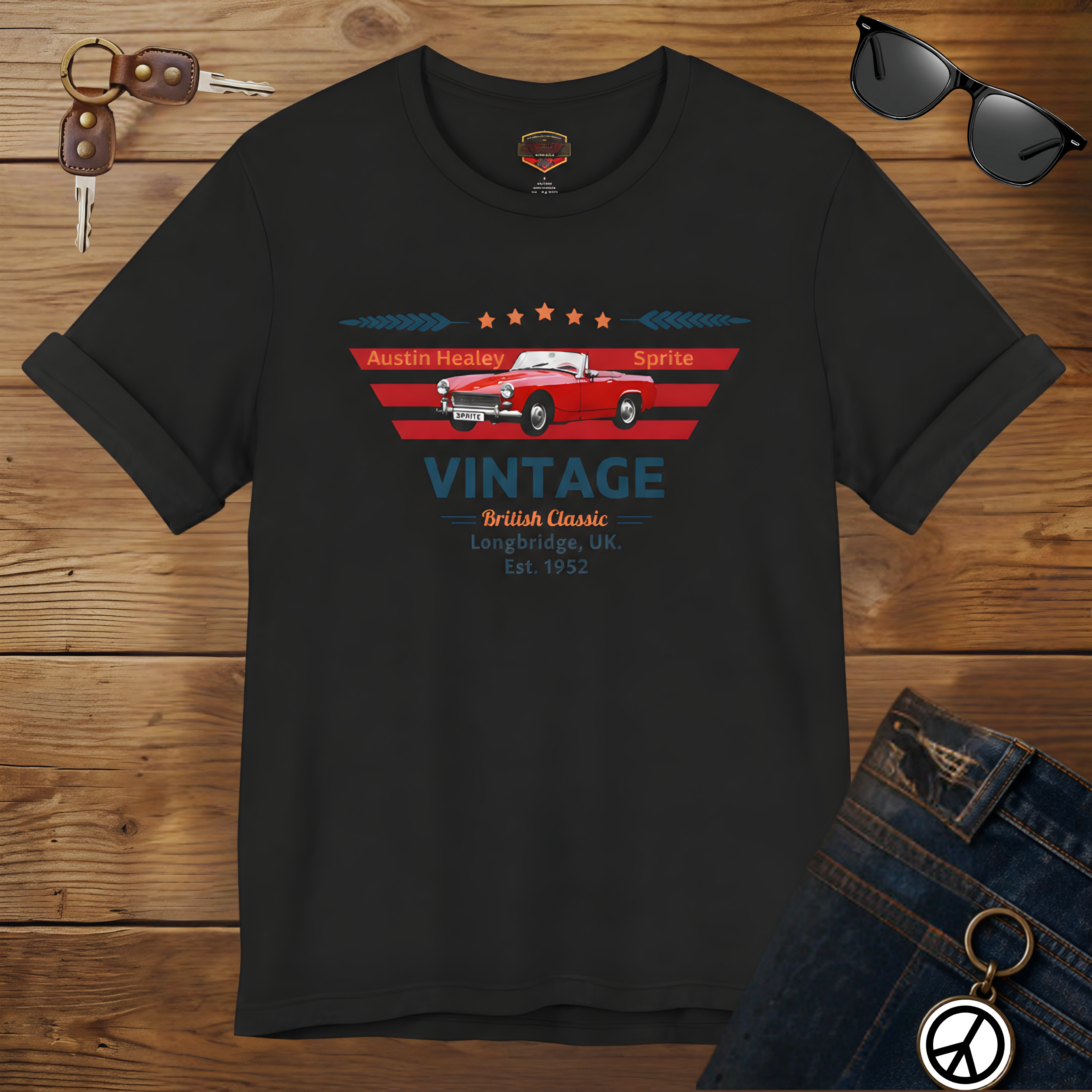 Black t-shirt with vintage car graphic on a wooden surface with sunglasses and jeans.
