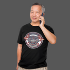 Man wearing a black t-shirt with a graphic Healey Sprite design, talking on a phone against a gray background