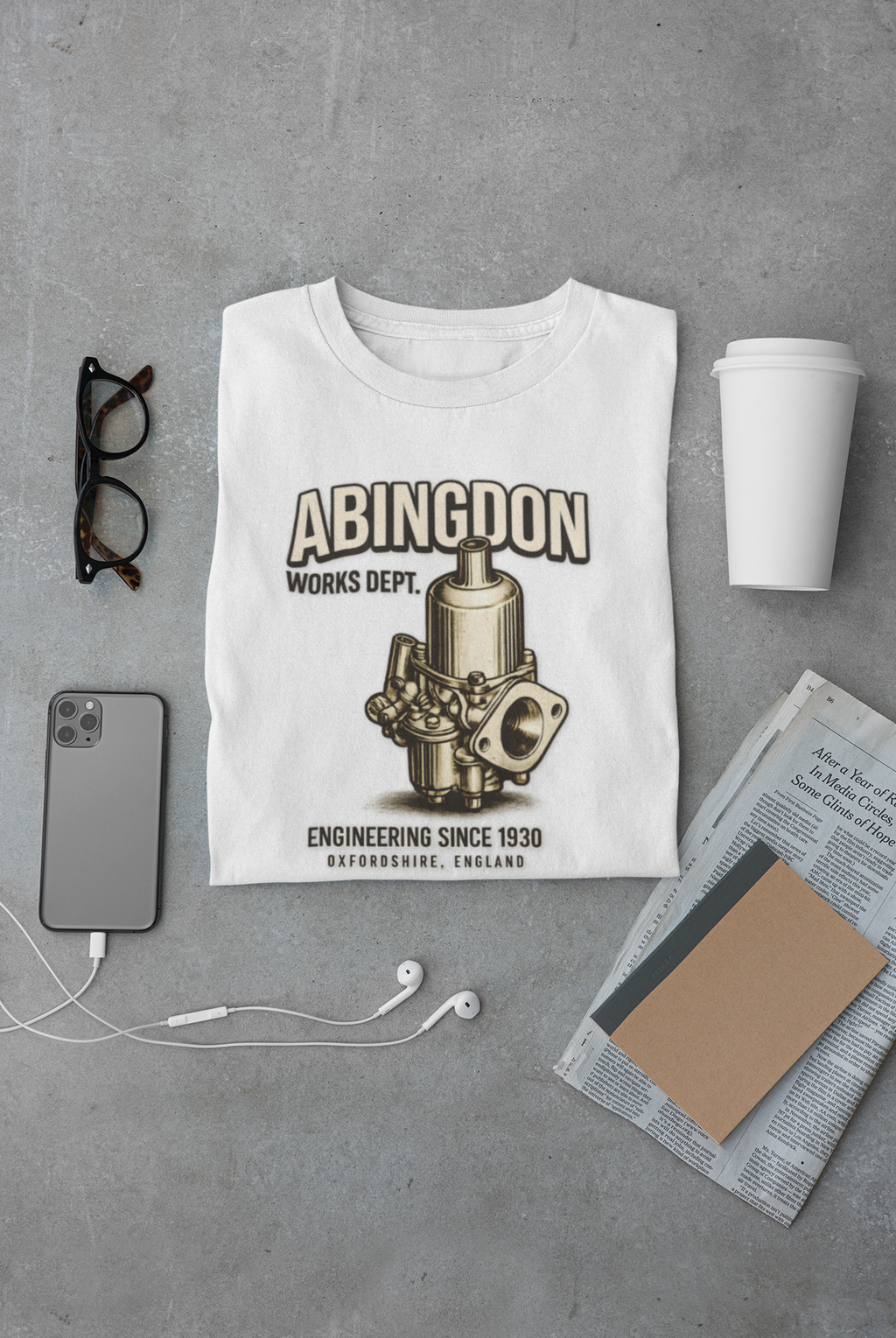 White t-shirt with 'Abingdon Works Dept.' graphic on a gray surface with phone, glasses, and cup.