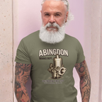 Man wearing a military green t-shirt with 'Abingdon Works Dept.' design against a light pink wall.