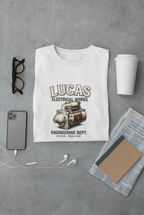 White t-shirt with 'Lucas Electrical Works' design on a gray surface with accessories.