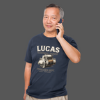 Man wearing a navy blue t-shirt with Lucas Electrical Works graphic and text, talking on a phone against a gray background