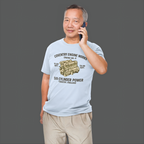 Man wearing a light blue t-shirt with an 'Coventry Engine Works'  graphic and text, talking on a phone against a gray background