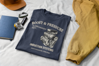 Navy blue t-shirt with supercharged engine graphic and text on a white surface with a tan colored jacket and a cap.