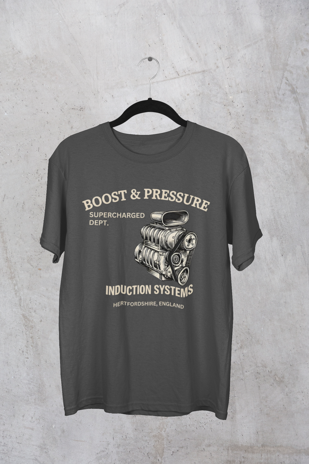 Gray t-shirt with supercharged engine graphic and text on a hanger against a concrete wall.