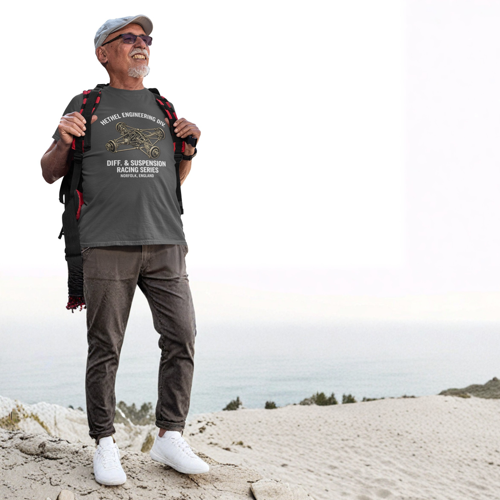 Man standing on a sandy hill wearing a dark heather t-shirt with text and graphics, brown pants, white shoes, and a backpack.