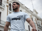Man wearing a light blue t-shirt with a Healey graphic and text in an urban setting