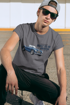 Man wearing a dark heather t-shirt with a Healey car graphic and text, sitting outdoors. 