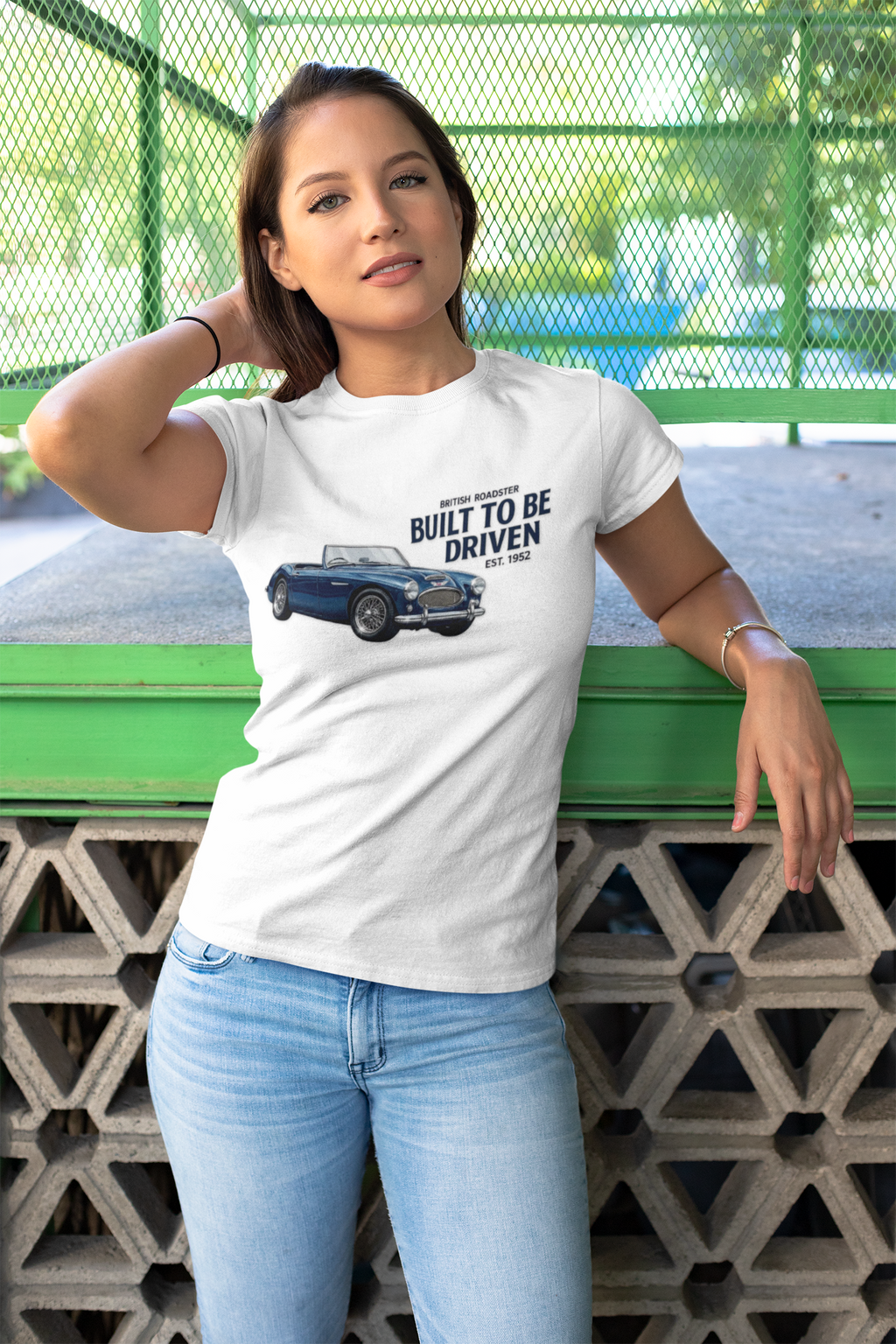 Woman wearing a white t-shirt with a graphic design and text, standing against a green metal fence.
