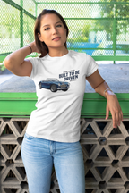 Woman wearing a white t-shirt with a graphic design and text, standing against a green metal fence.