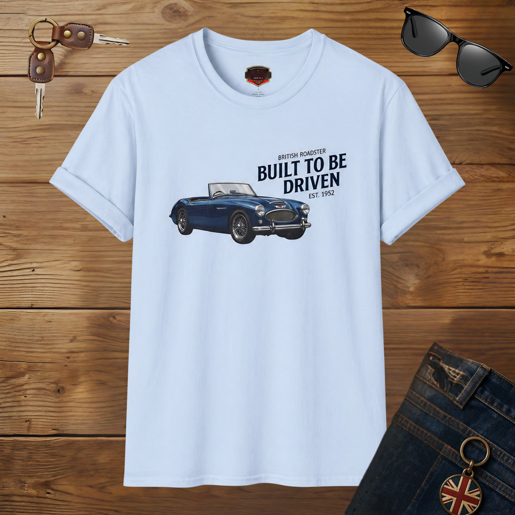 Light blue t-shirt with a Healey car graphic and text on a wooden surface with sunglasses and keys.