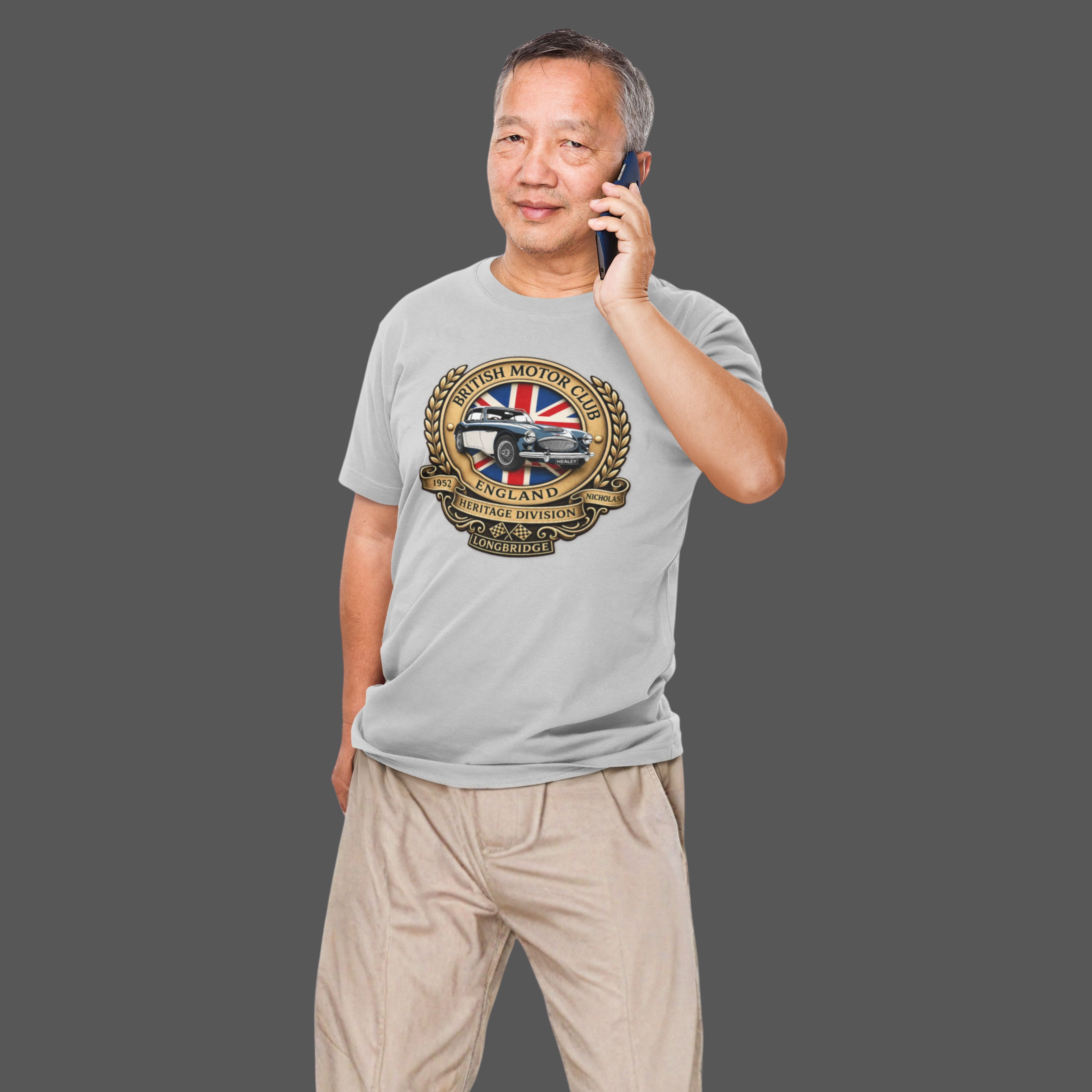 Man wearing a sport gray t-shirt with a British Motor Union logo, talking on a phone against a gray background