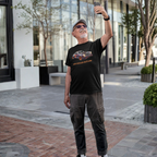 Model wearing the Healey Threads 'Air Cooled Outlaw' premium graphic tee in a relaxed outdoor urban setting - showcasing the vintage automotive design on a classic black tee.