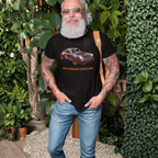 Man wearing a black t-shirt with a colorful car graphic and text, standing outdoors among greenery.