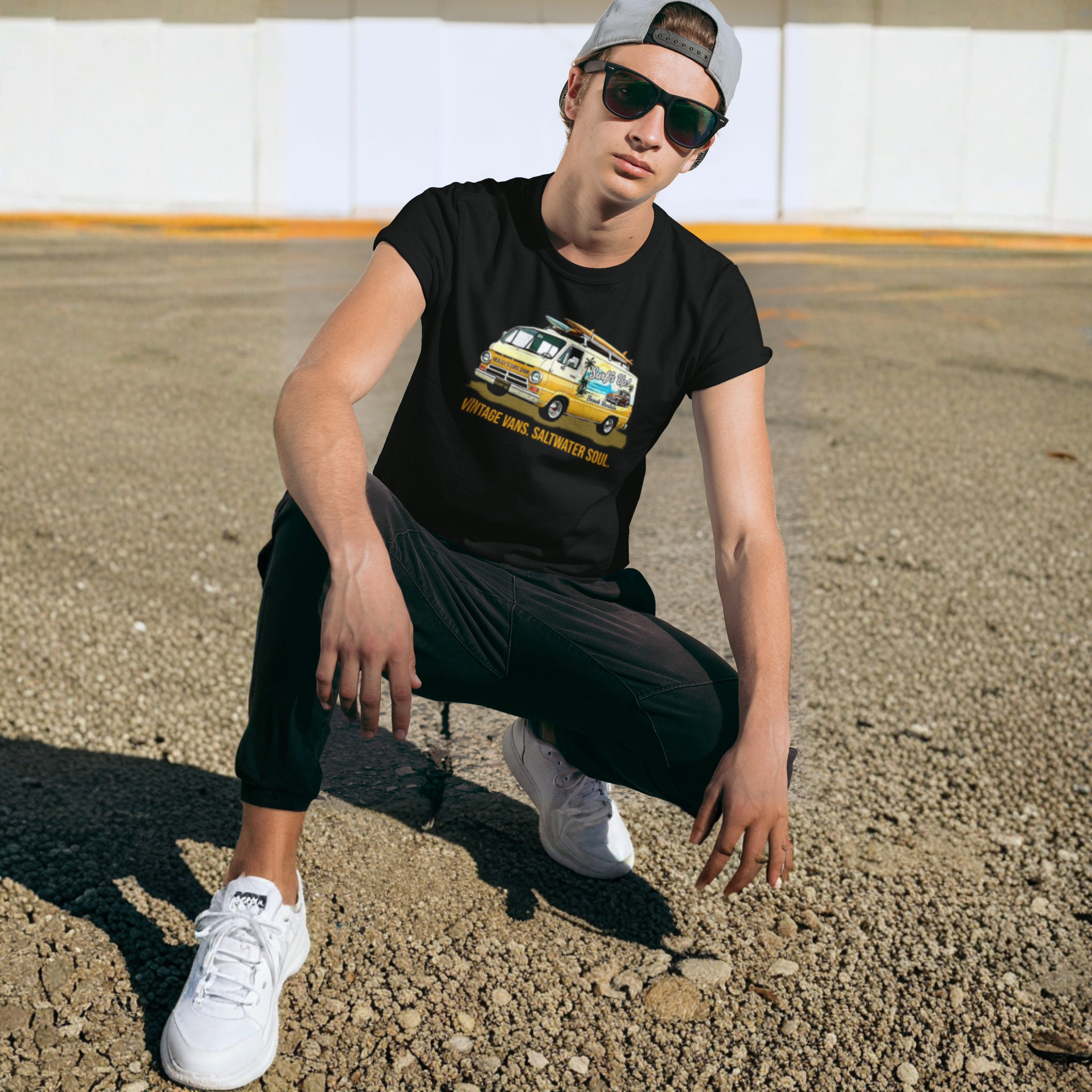 Man wearing a black t-shirt with a graphic classic van design, sunglasses, and a cap in an outdoor setting.