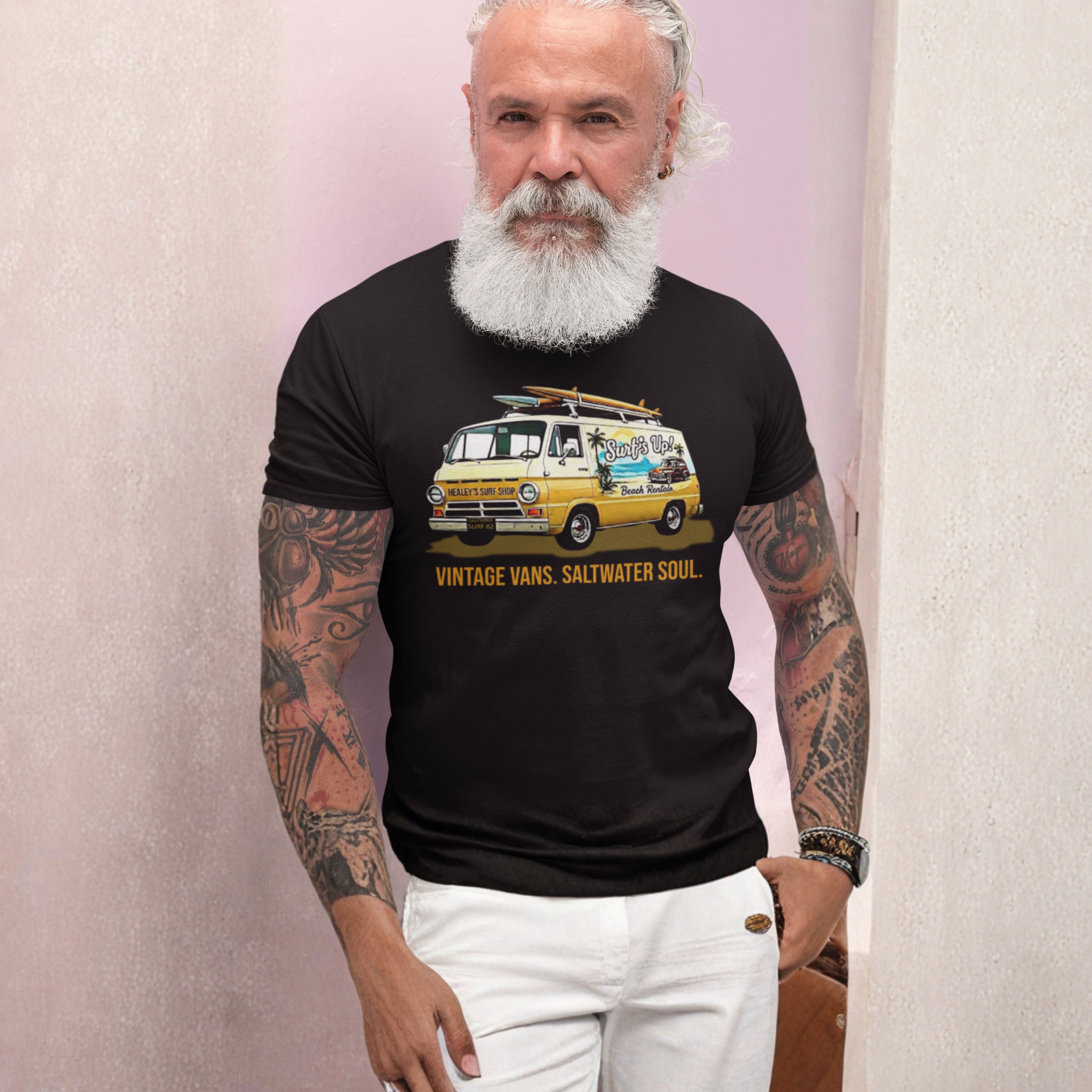 Man wearing a black t-shirt with a graphic design of a van and text, standing against a light pink wall.