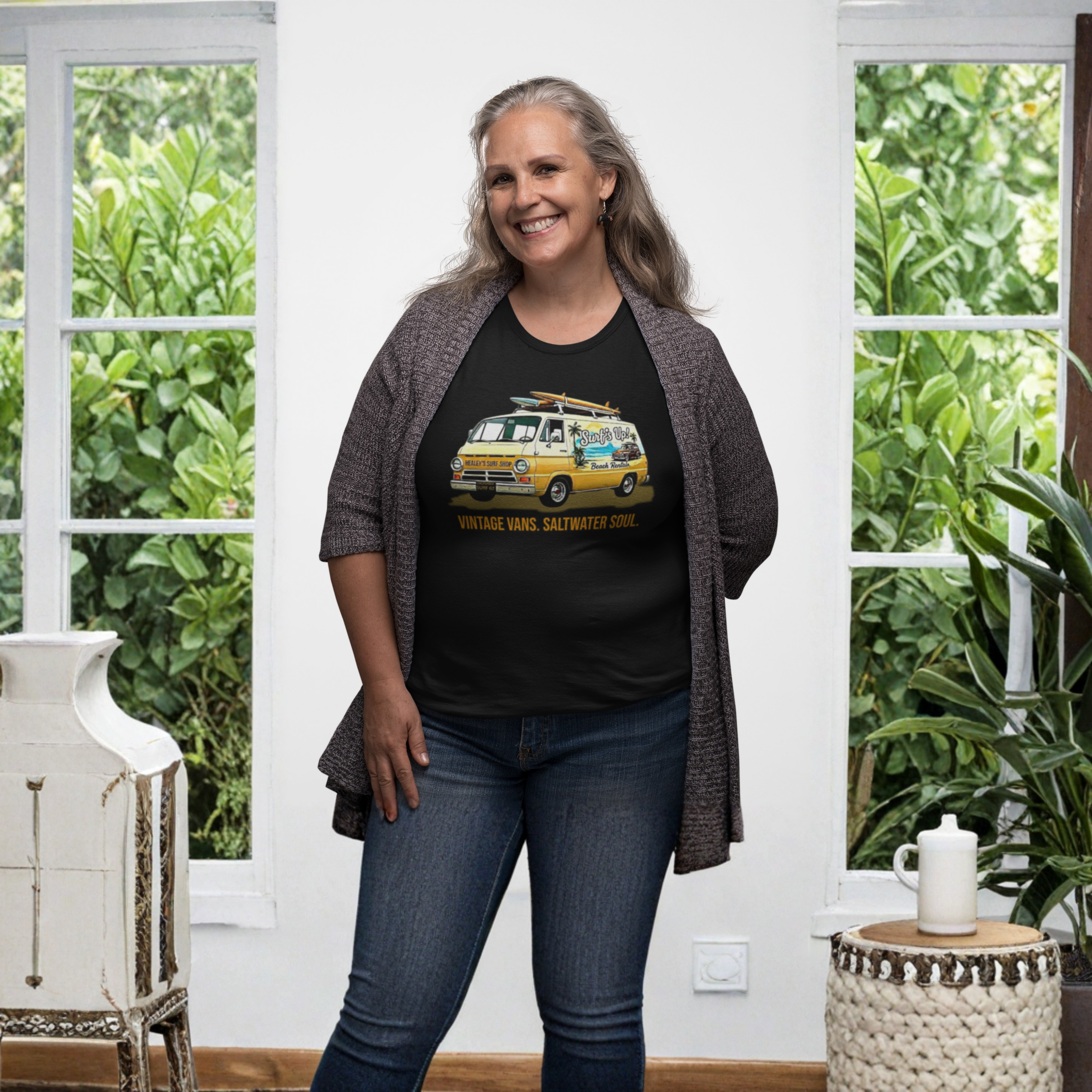 Woman wearing a black t-shirt with a vintage van graphic, standing in a room with plants and a white wall.