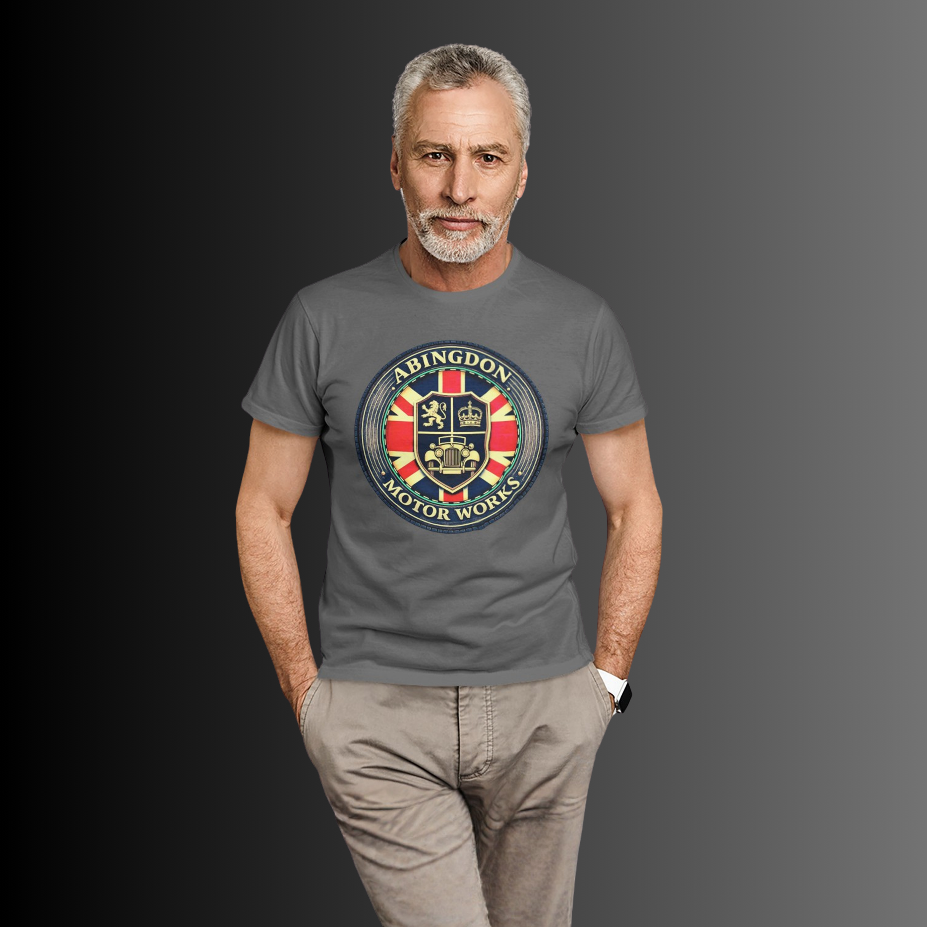 A man wearing a dark gray t-shirt with a circular 'Abingdon Motor Works' crest graphic on the chest, paired with beige trousers, set against a dark gray gradient background.