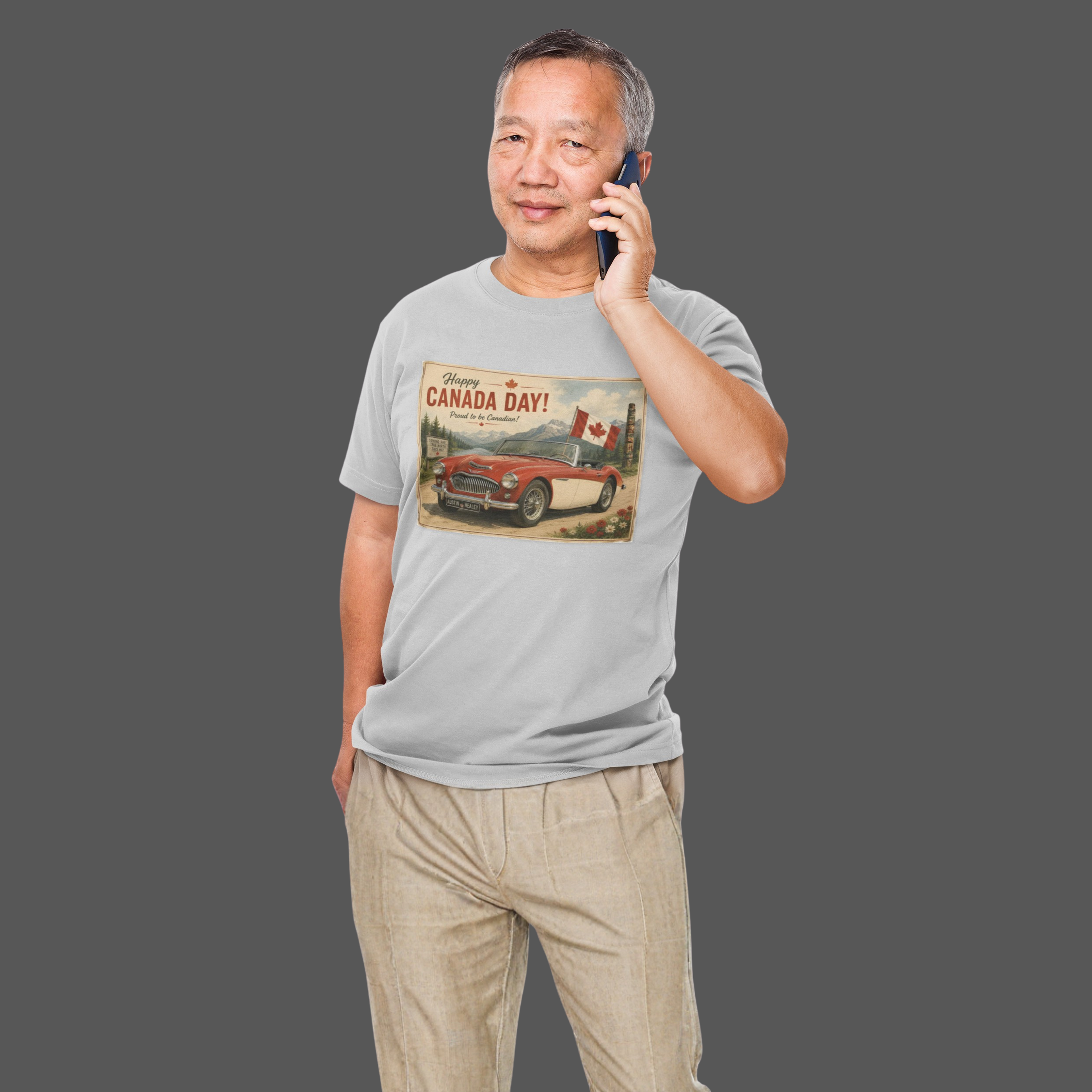 A man wearing a sport gray t-shirt with a vintage-style 'Canada Day' graphic print featuring a red car and Canadian flag, standing against a solid dark gray background.