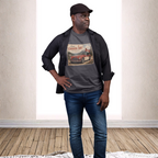 A man modeling a dark gray graphic t-shirt with a vintage Canadian car print, styled with a black button-up shirt, blue jeans, and a black cap in a bright room with a wood floor.