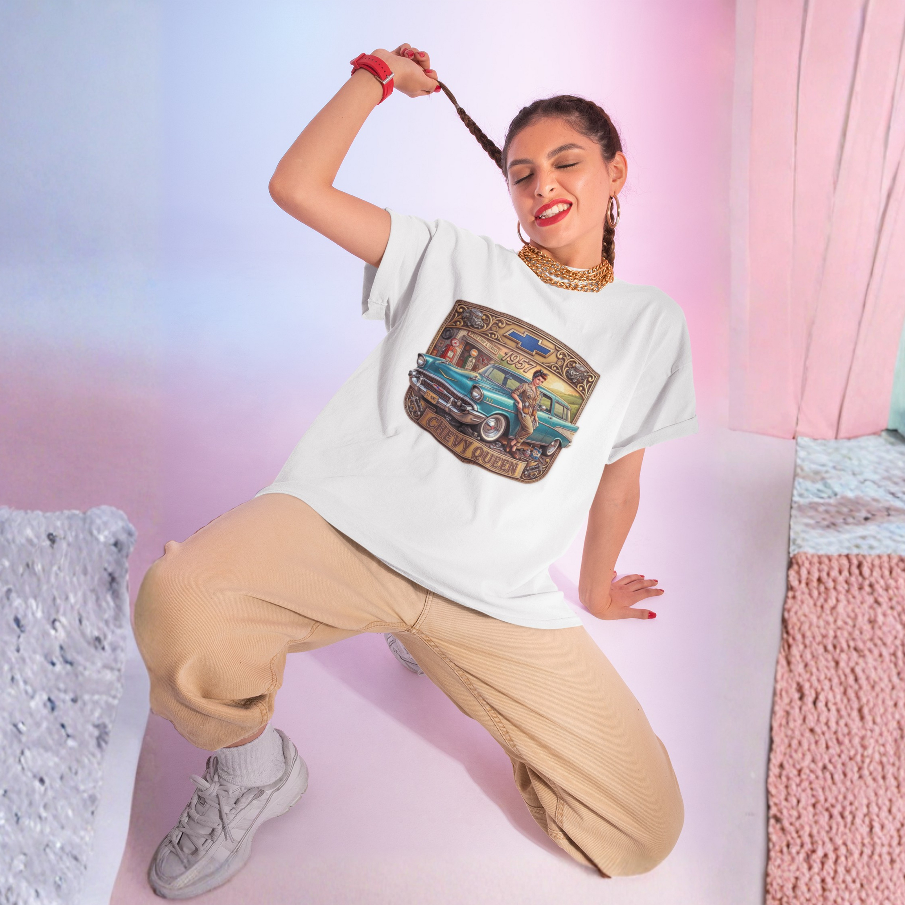 A woman poses in a white graphic t-shirt featuring a vintage teal car illustration, paired with beige cargo pants and white sneakers, set against a pastel pink and blue studio background.
