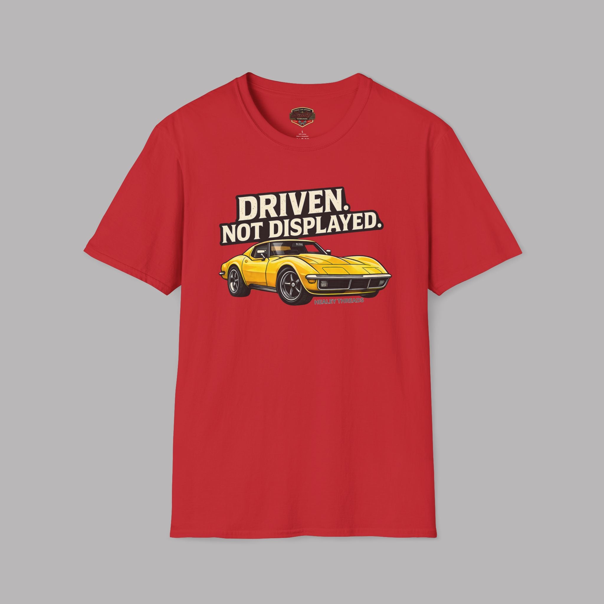 Red t-shirt with a yellow muscle car graphic and text 'Driven. Not Displayed.' on a gray background