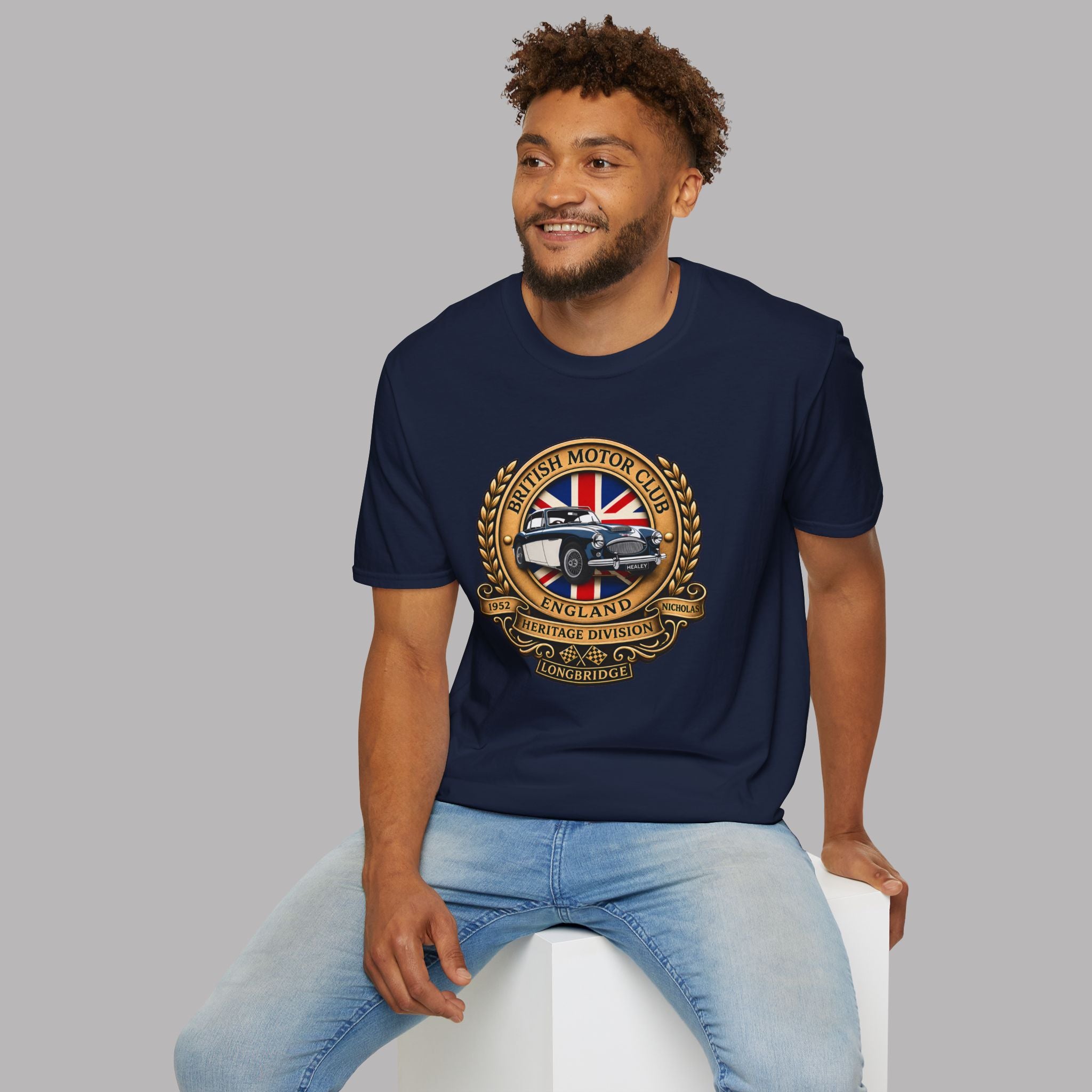 Man wearing a navy blue t-shirt with a British Motor Club logo and text, sitting on a white stool against a gray background.