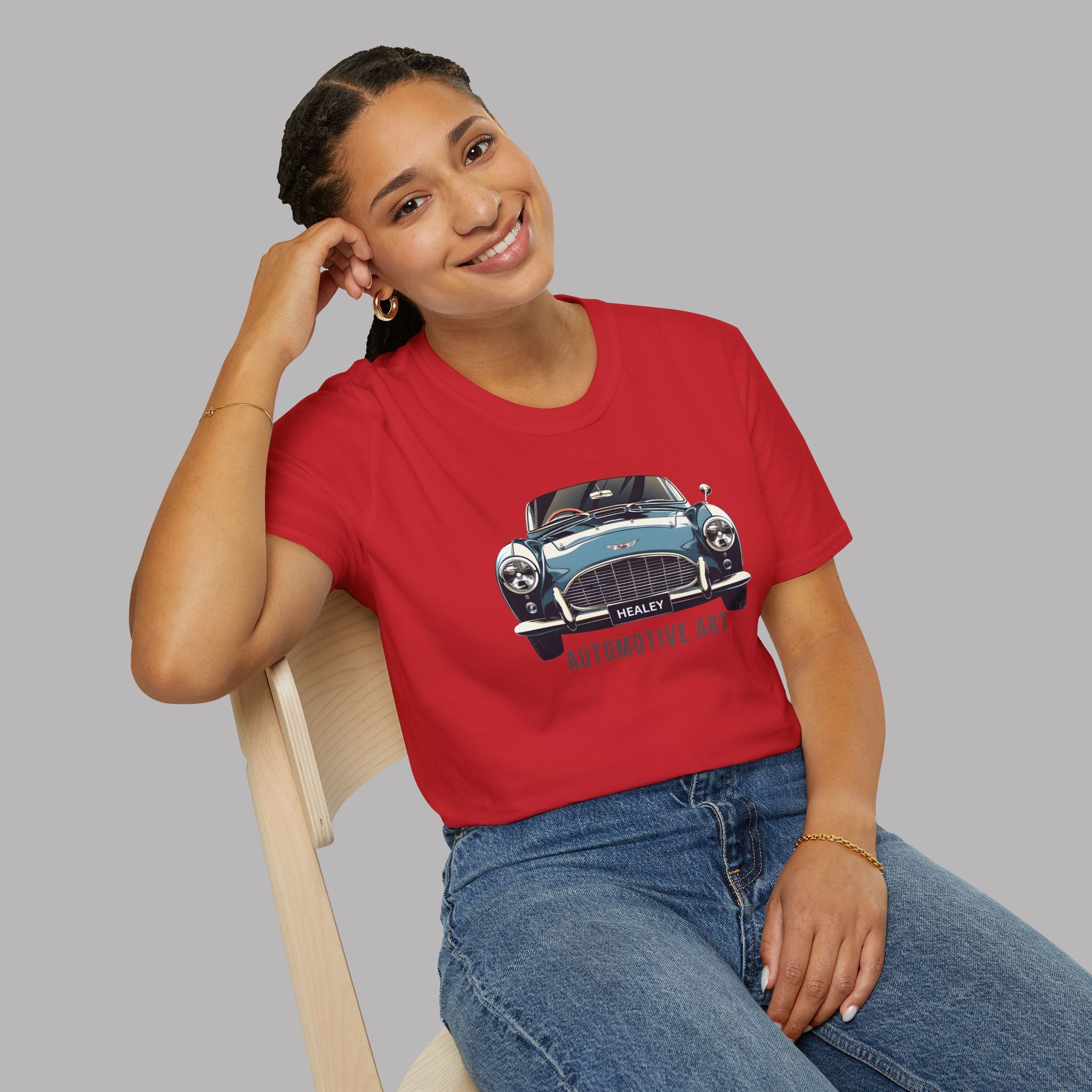 Woman wearing a red t-shirt with a Healey car graphic, sitting on a chair against a gray background