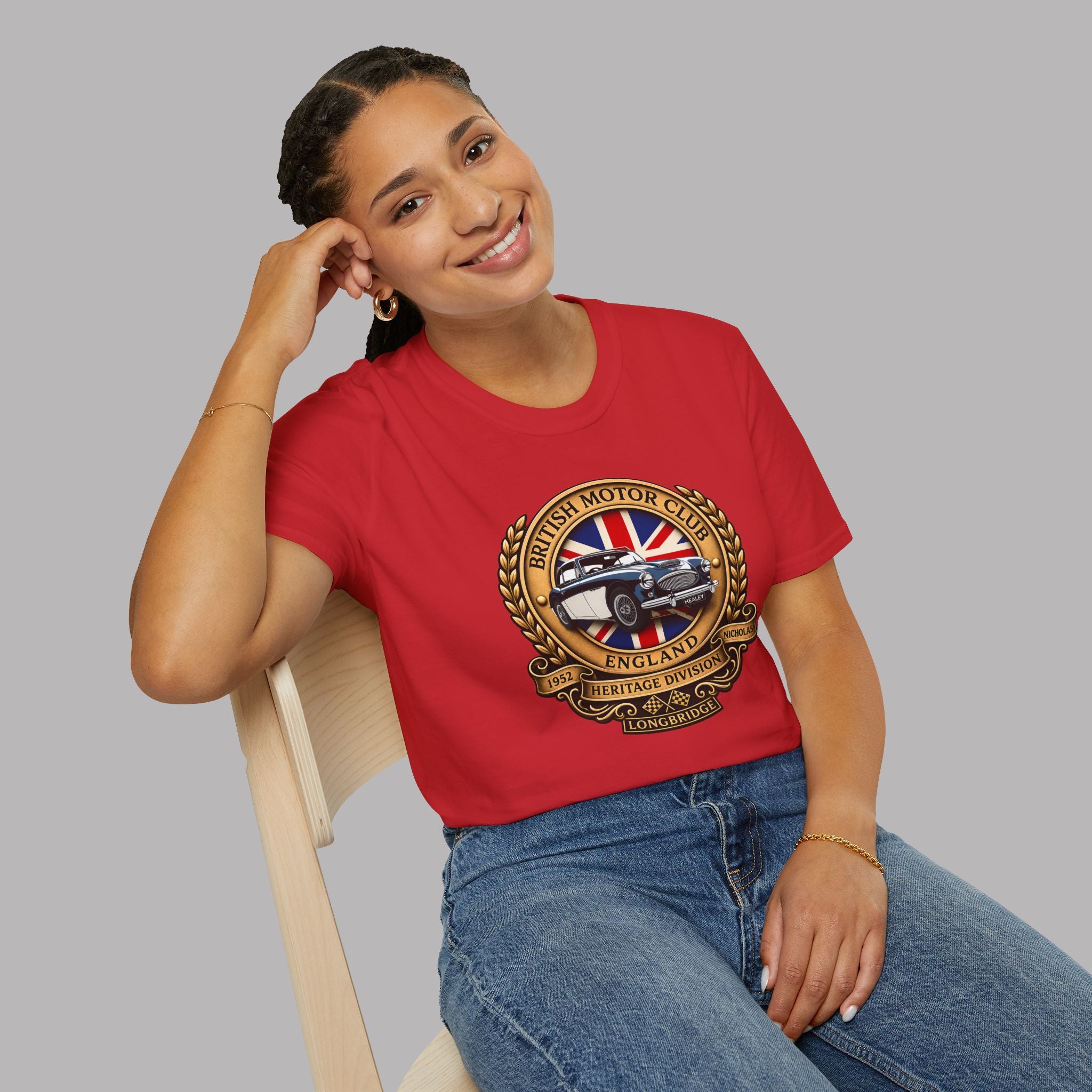 Woman wearing a red t-shirt with a British Motor Club logo, sitting on a chair against a gray background.