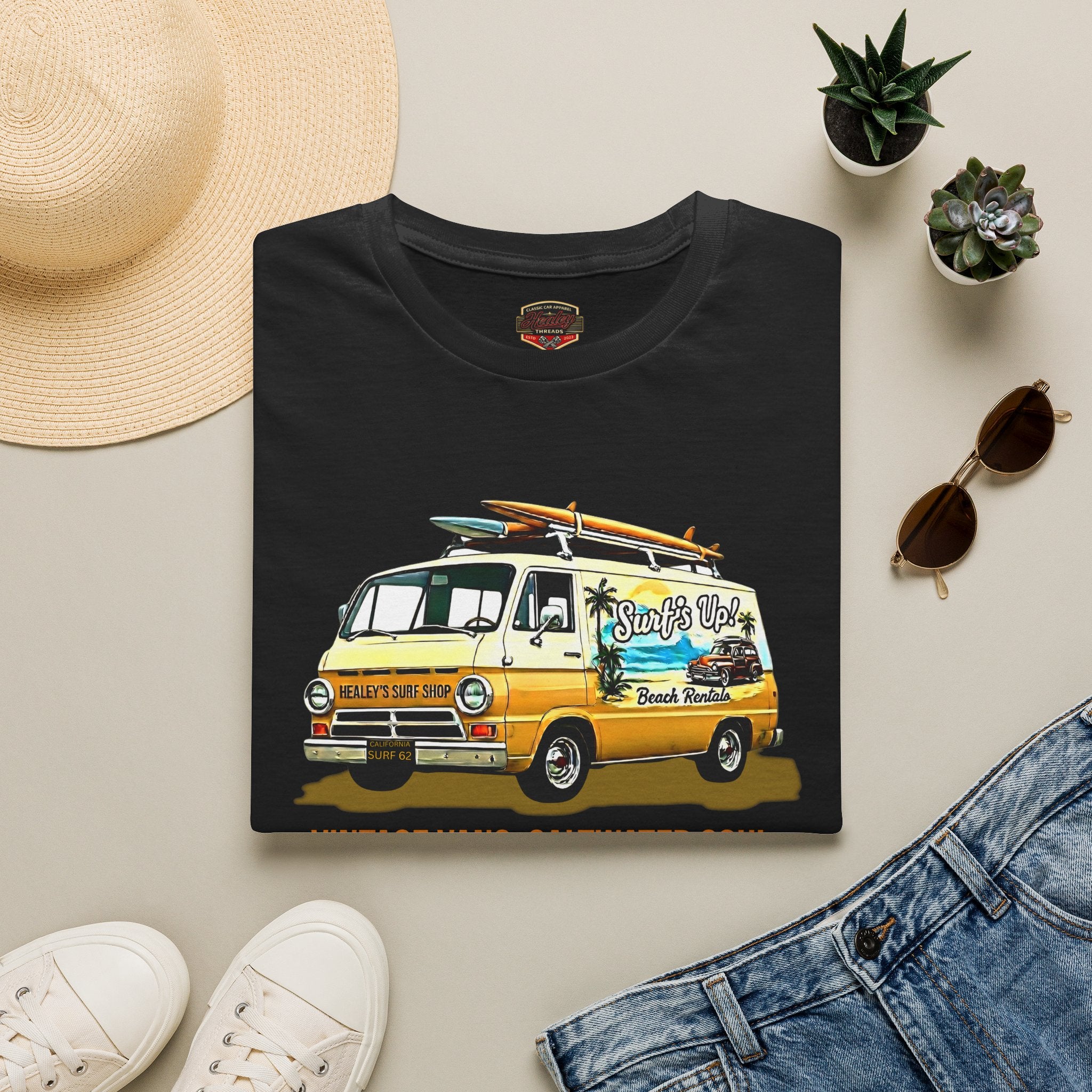Black t-shirt with a classic van graphic on a beige surface with accessories like a hat, sunglasses, and jeans.