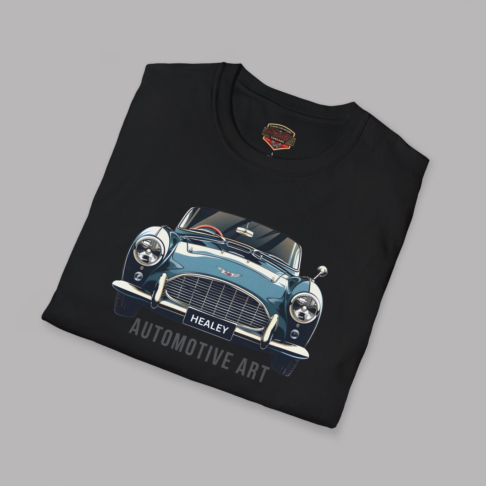 Folded black t-shirt with a vintage car graphic and 'Healey Automotive Art' text on a gray background