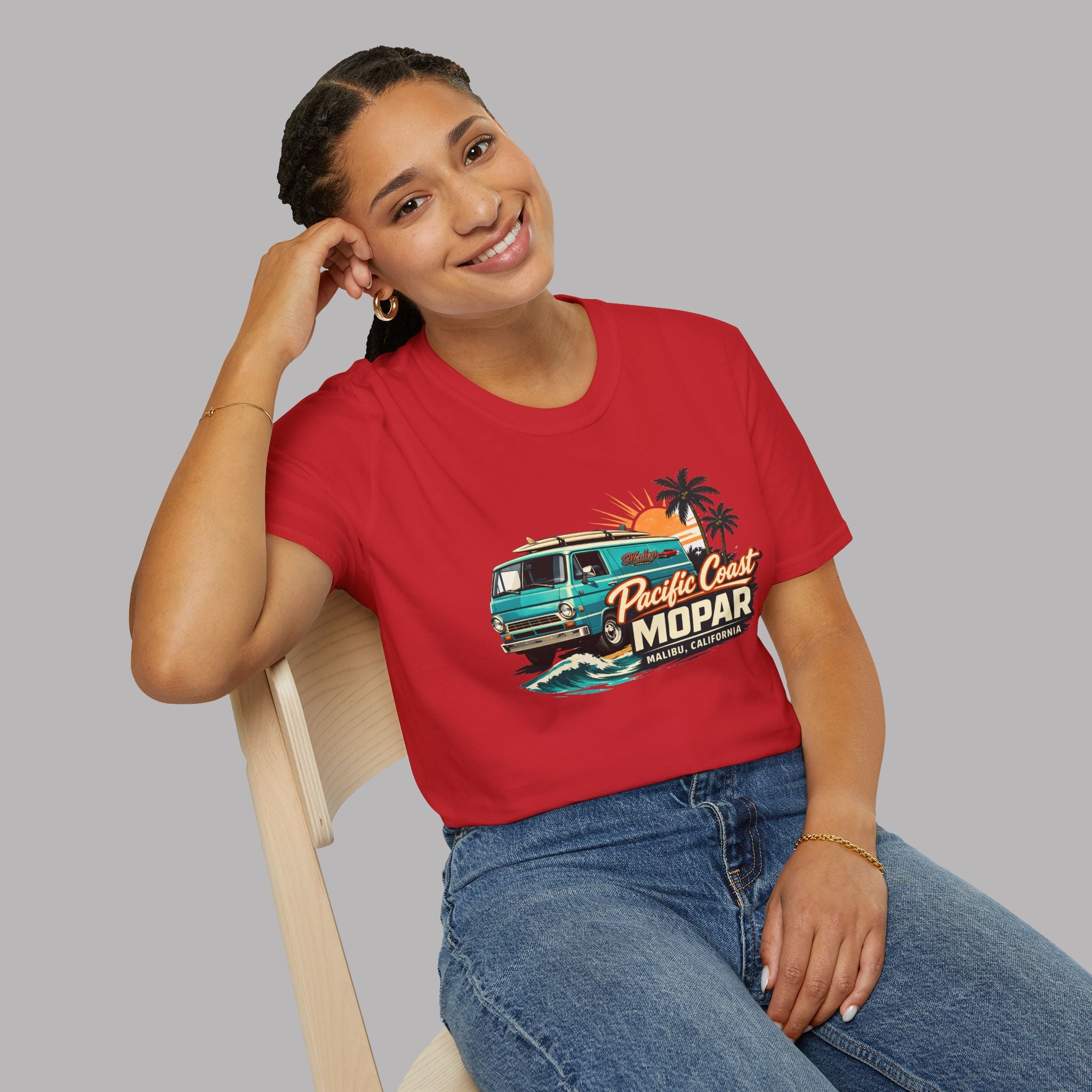 Woman wearing a red t-shirt with a graphic van design sitting on a chair against a gray background
