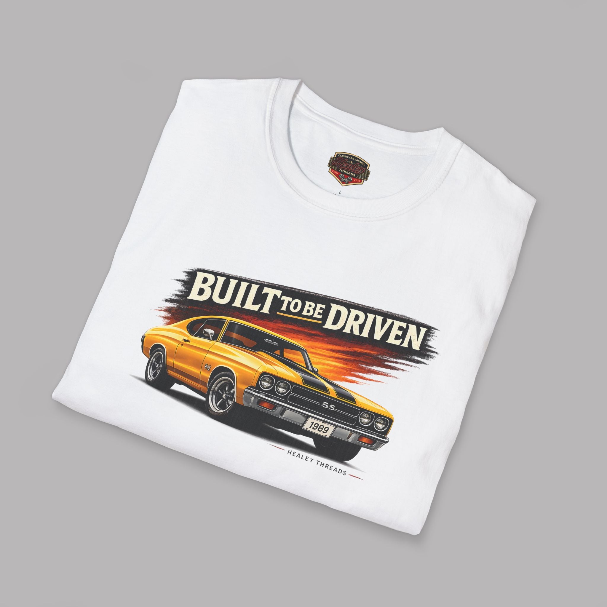 Folded white t-shirt with a graphic of a car and 'Built to be Driven' text on a gray background