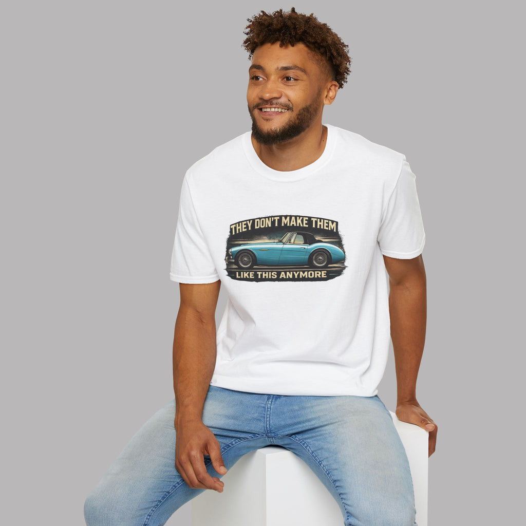 Man wearing a white t-shirt with a Healey graphic design sitting on a white stool against a gray background