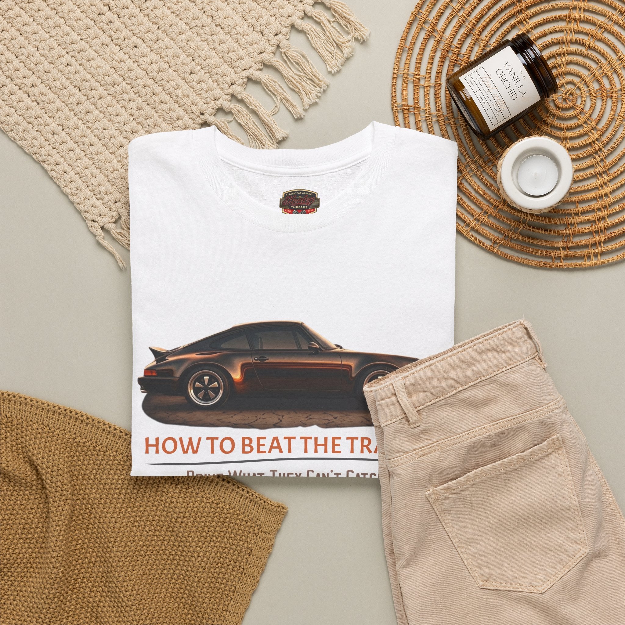 White t-shirt with classic car graphic and text, beige pants, and decorative items on a neutral background