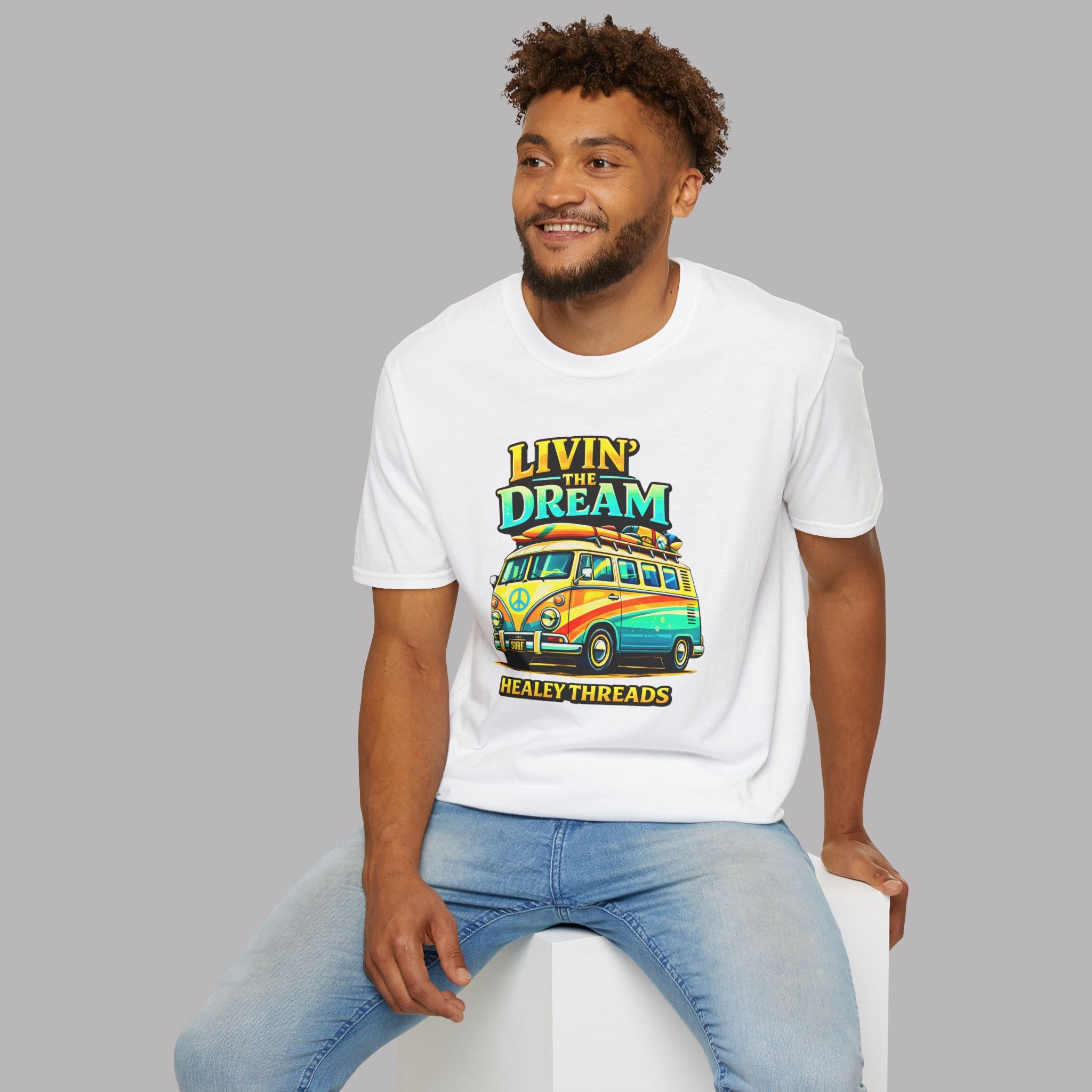 Man wearing a white t-shirt with a colorful van graphic and text, sitting on a white stool against a gray background.