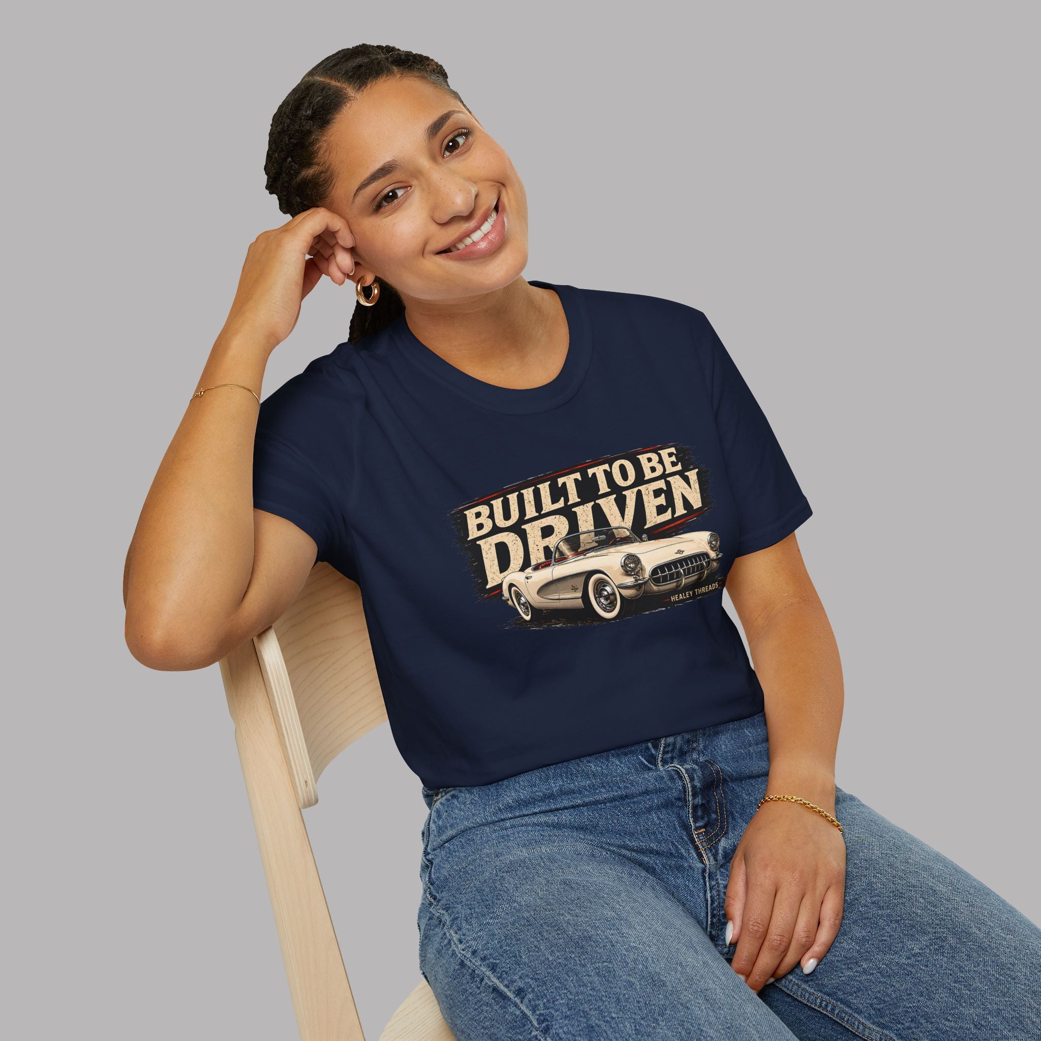 Woman wearing a navy blue t-shirt with 'Built to be Driven' graphic sitting on a chair.
