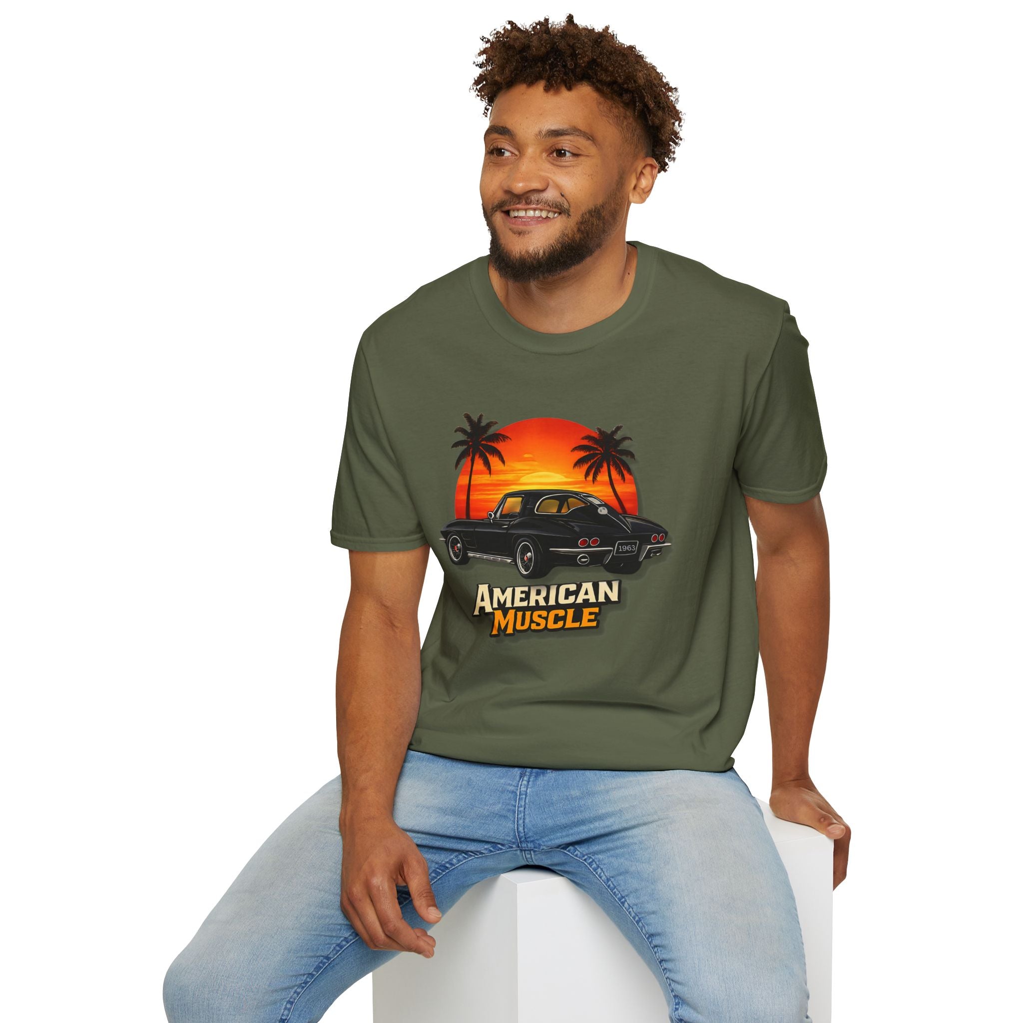 Man wearing a military green t-shirt with a graphic design of a car and palm trees, sitting on a white stool.