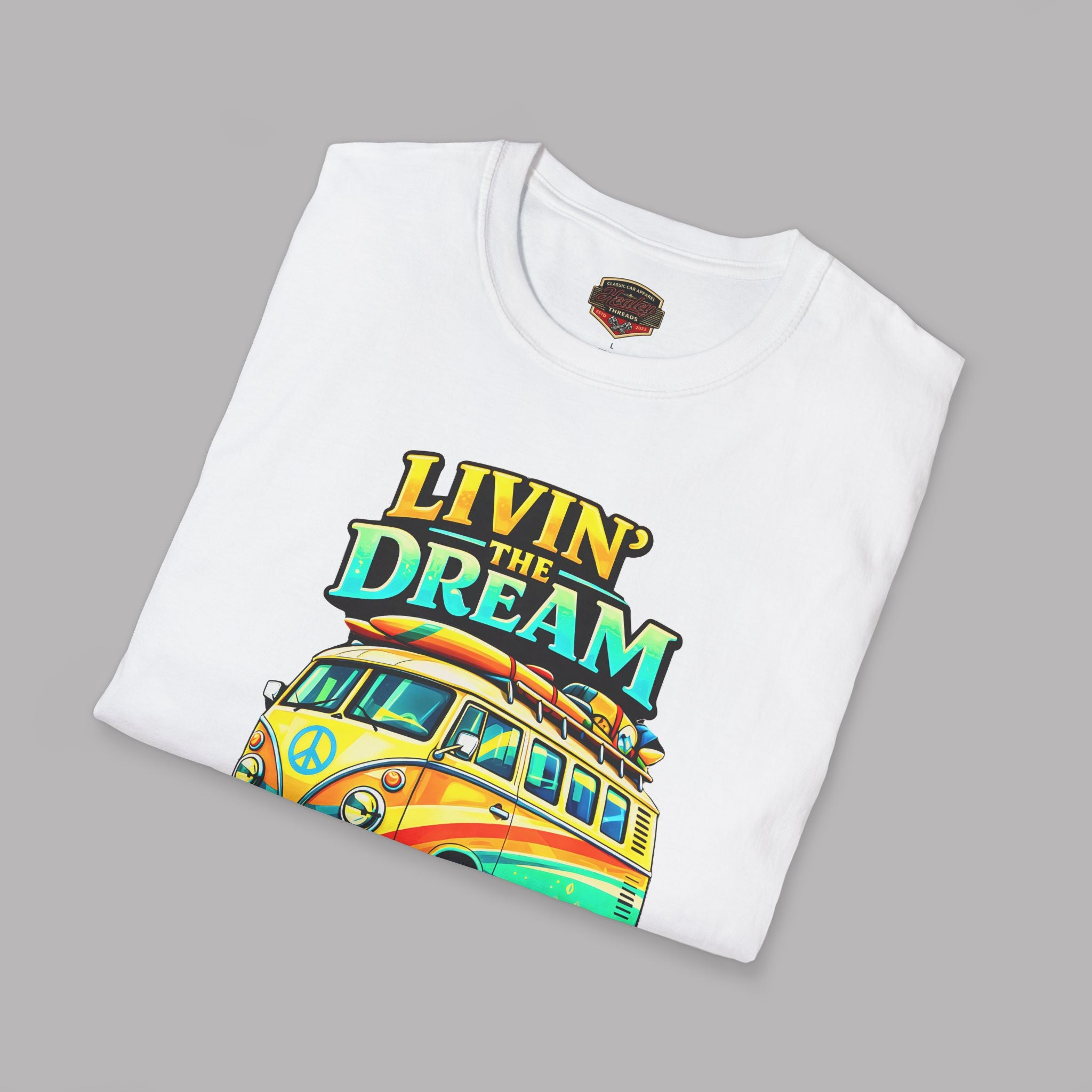 Folded white t-shirt with 'Livin' the Dream' graphic  design featuring a van and rainbow colors on a gray background.