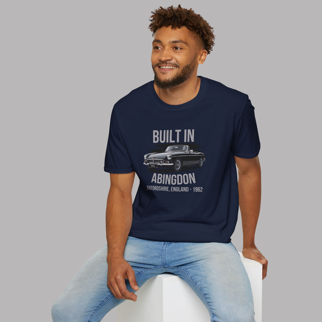 Man wearing a navy blue t-shirt with a classic car graphic and text, sitting on a white stool against a gray background.
