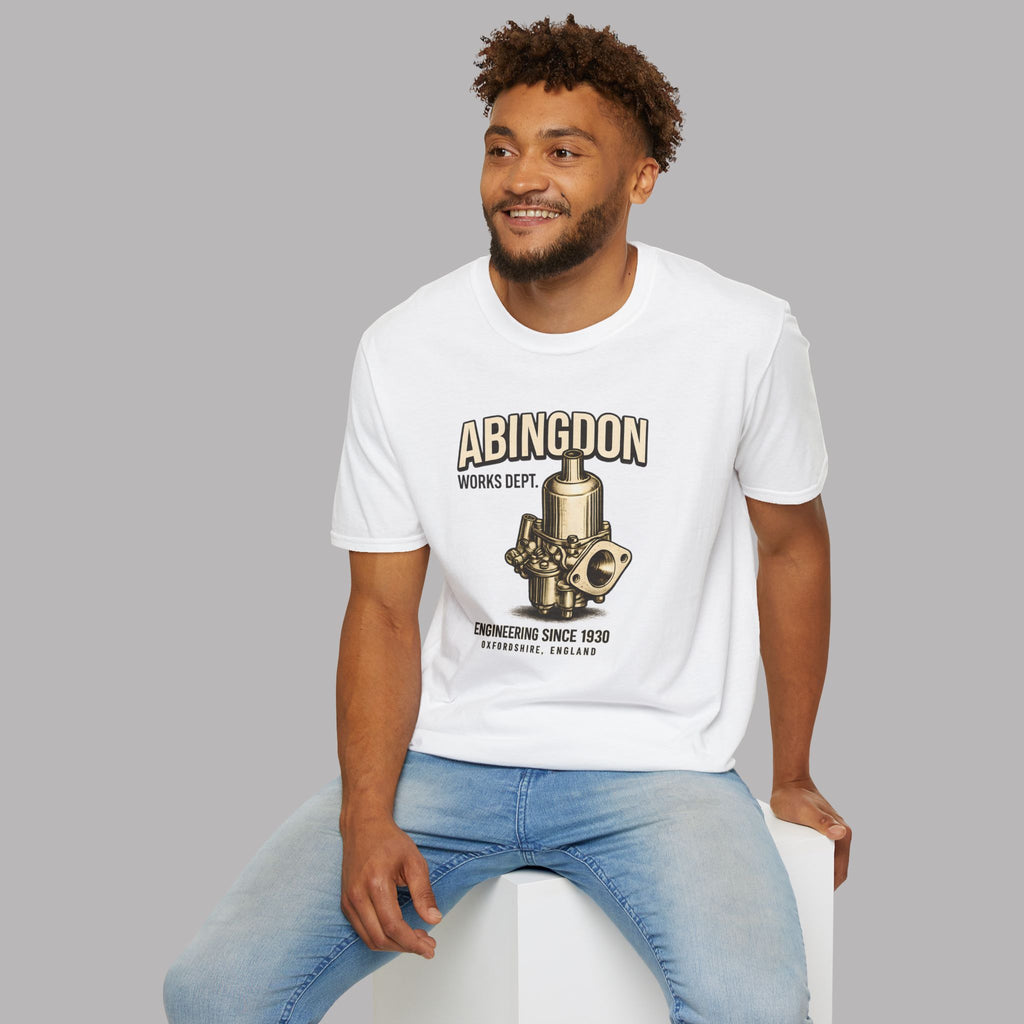 Man wearing a white t-shirt with a 'Abingdon Works Dept.' graphic design and text, sitting on a white stool against a gray background.
