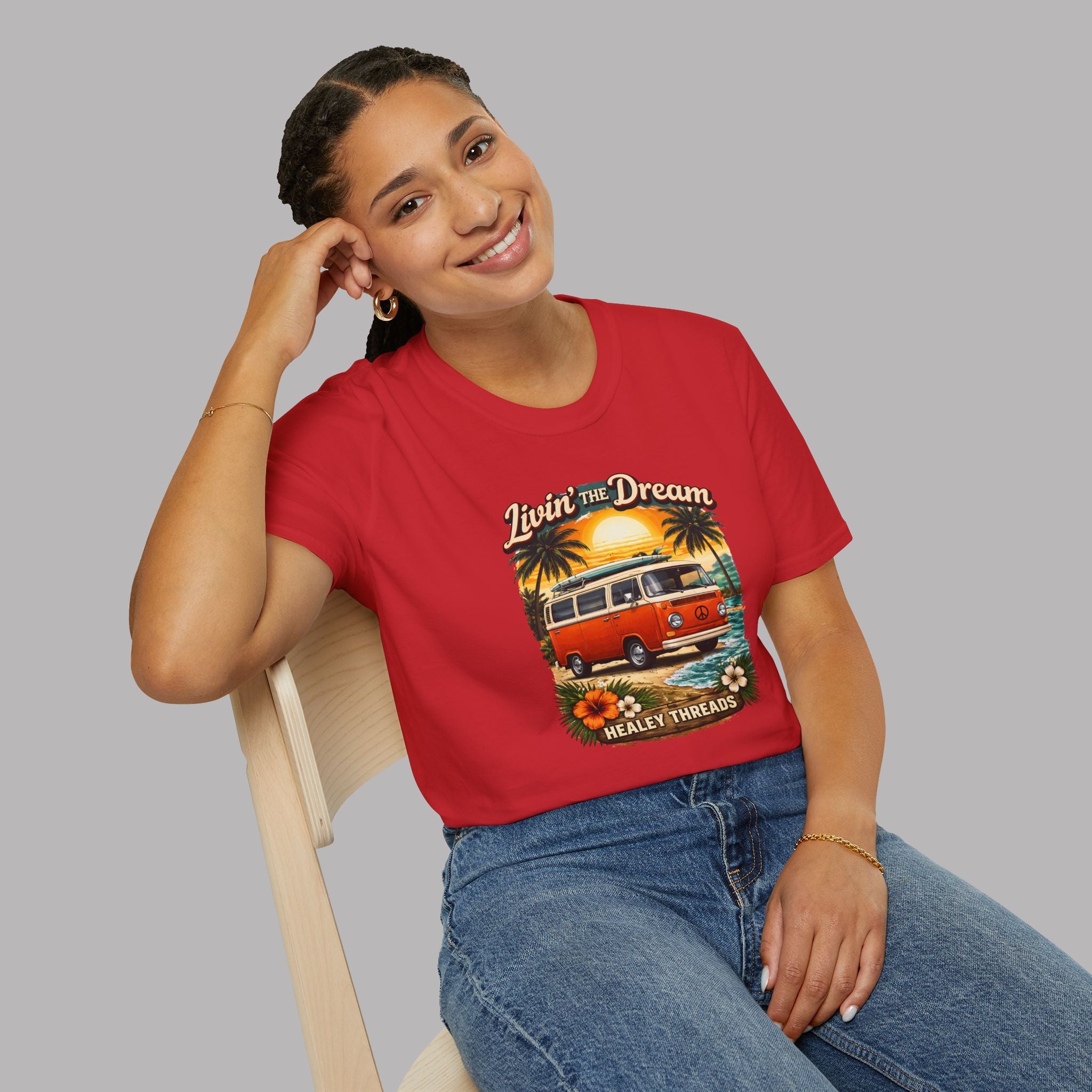 Woman wearing a red t-shirt with a graphic design of a van and text, sitting on a chair against a gray background.