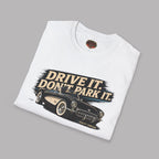 Folded white t-shirt with a vintage car graphic and text 'Drive It. Don't Park It.' on a gray background