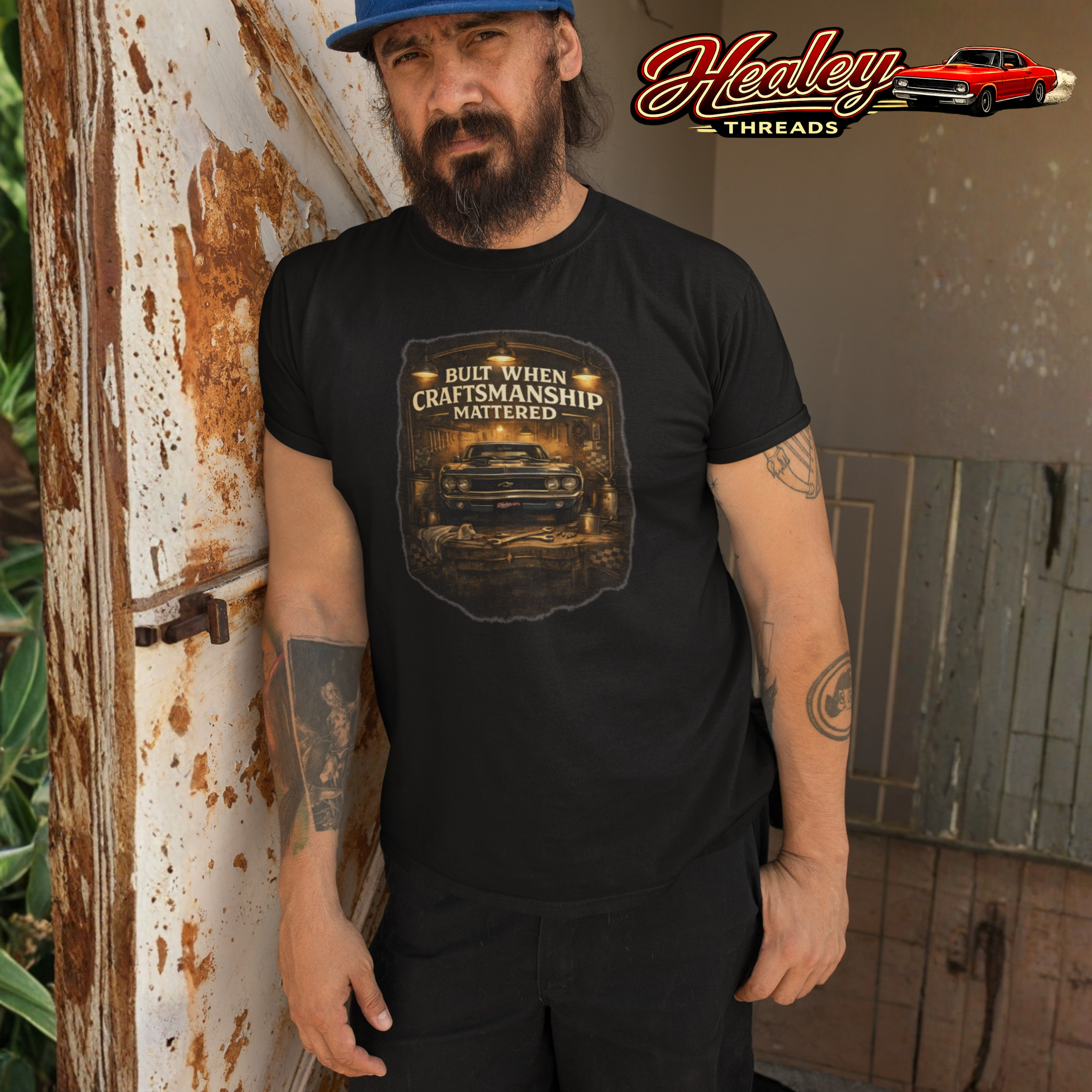 Man wearing a black t-shirt with a graphic design and text, standing next to a rustic wall.