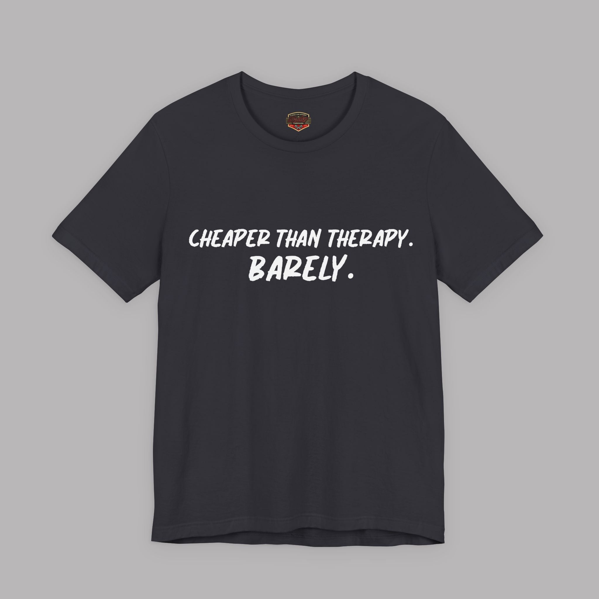 Dark gray t-shirt with white text "Cheaper than therapy. Barely." on a gray background