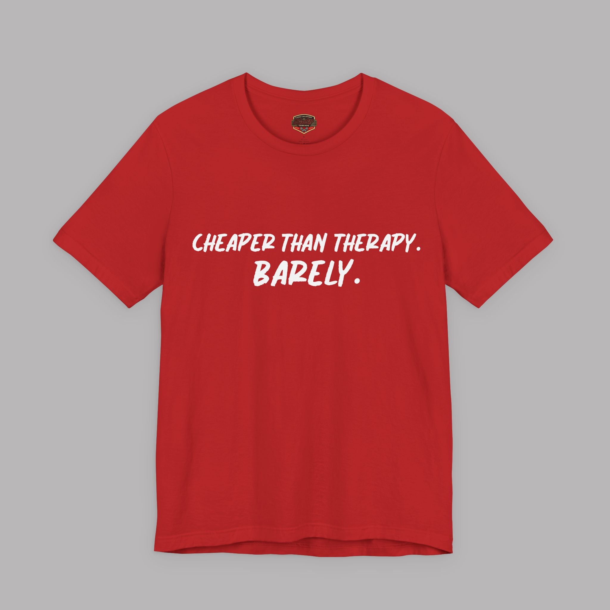 A red short-sleeve crewneck t-shirt with the text 'CHEAPER THAN THERAPY. BARELY.