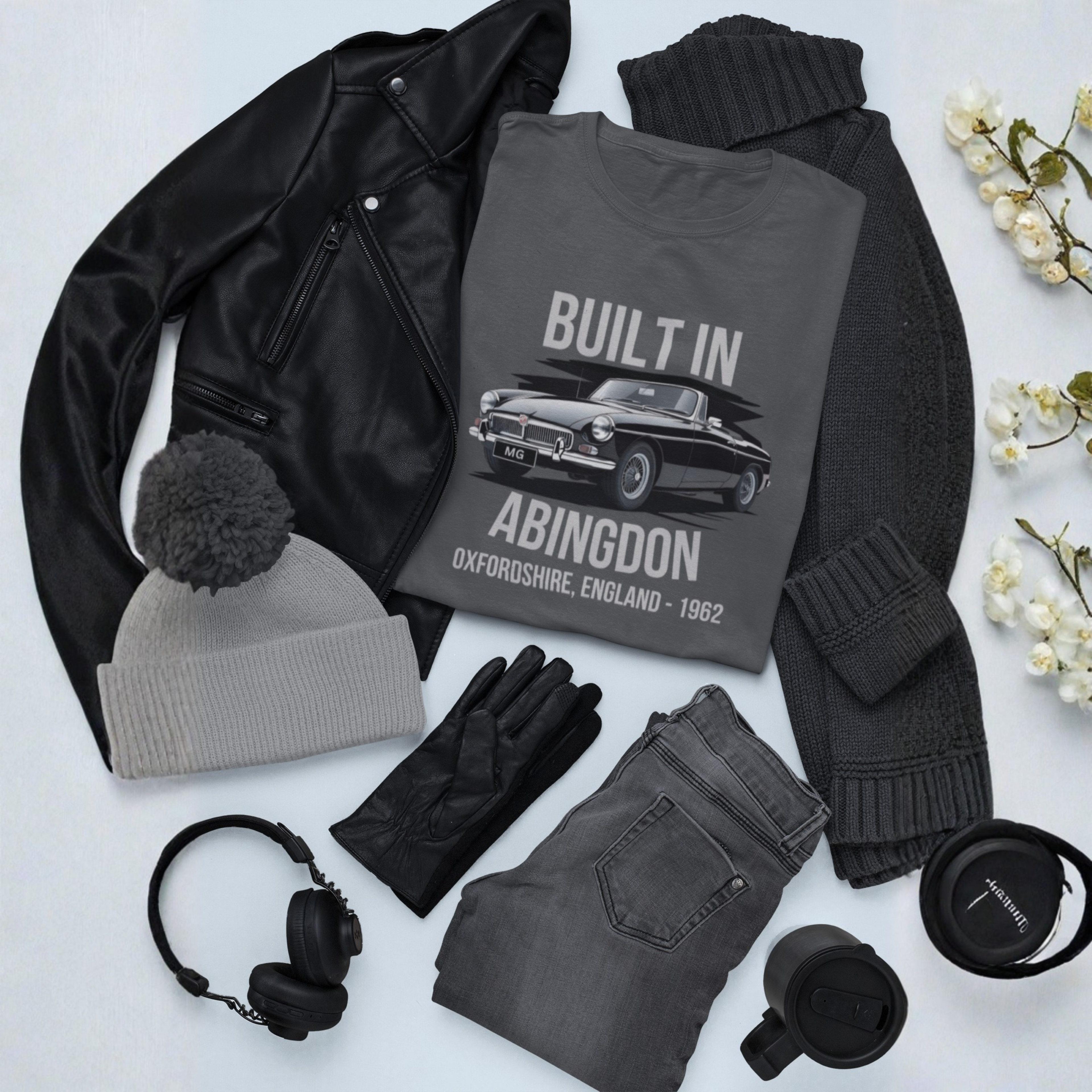 Collection of clothing and accessories including a gray t-shirt with 'Built in Abingdon' design, black jacket, gray beanie, gloves, jeans, headphones, and a mug on a light background.