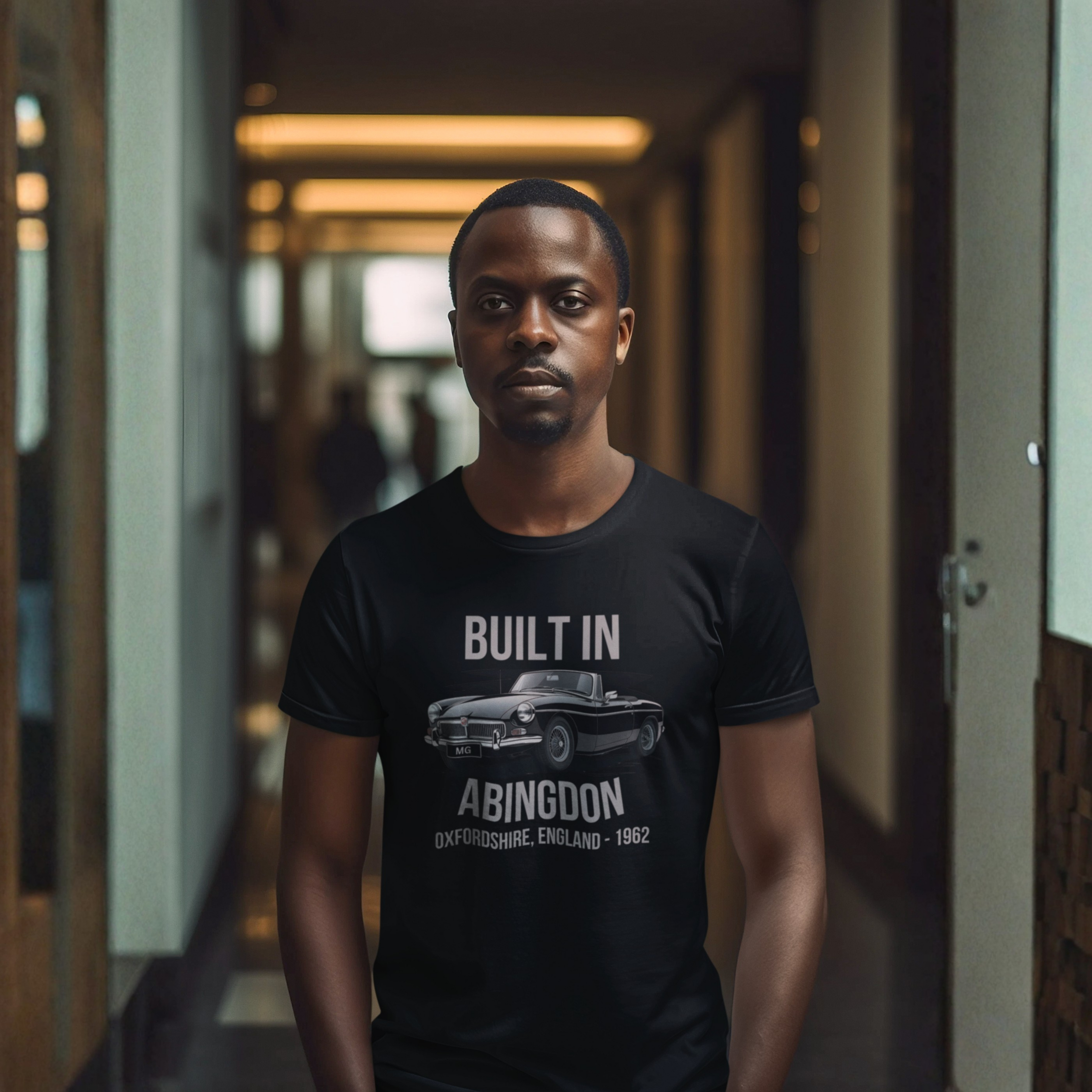 Man wearing a black t-shirt with a graphic MGB car design and text in a hallway.